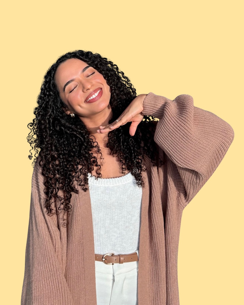 Greisy Milena sonriendo con cardigan beige sobre fondo amarillo